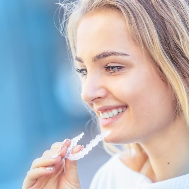 Smiling blonde woman holding clear oral appliance